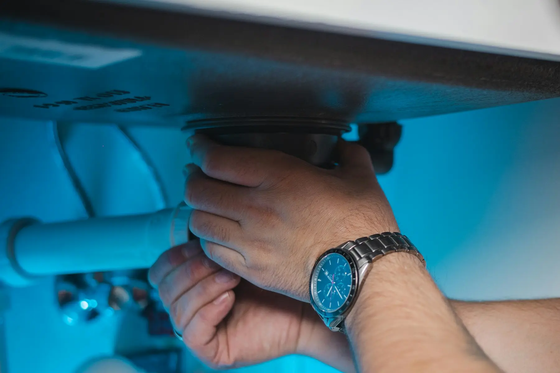Hands tightening a drain fitting under a sink