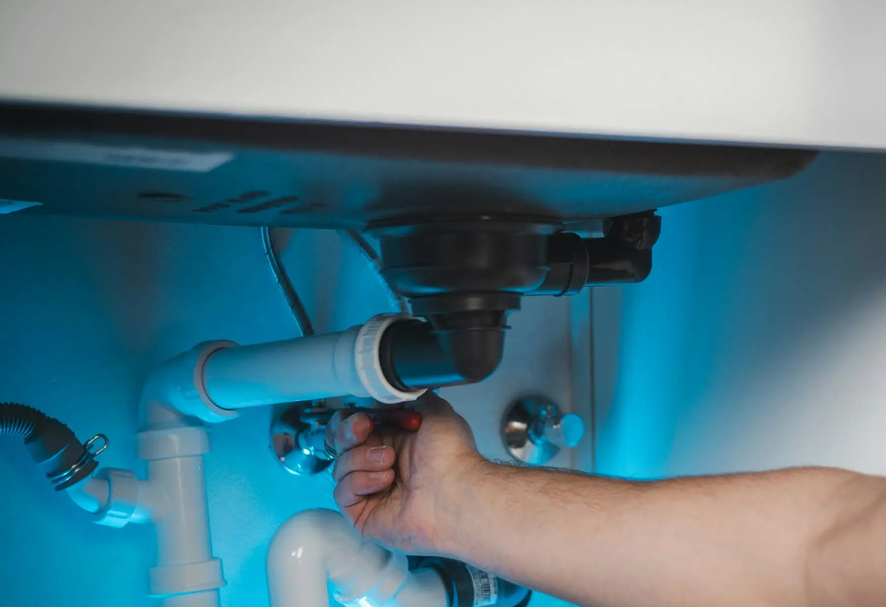 A hand working on a sink trap and shutoff valves